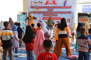 Tegal, Endonezya - 28 Temmuz 2024: Bir sunucu çocukları Brebes, Central Java, Endonezya 'daki kütüphane salonuna jimnastik yapmaya davet ediyor. Birlikte çalışmadan önce daha rahat olmak için egzersiz yapılır.