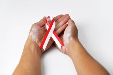 A person's hand holds a red and white ribbon forming a symbol of concern for fellow humans. This gives a message of awareness on World Cancer Day