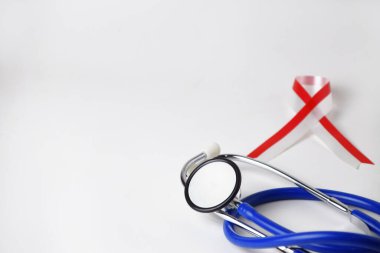 Dünya kanser gününü anmak için izole edilmiş beyaz arka planda bir doktor steteskobu ve kırmızı ve beyaz bir kurdele.