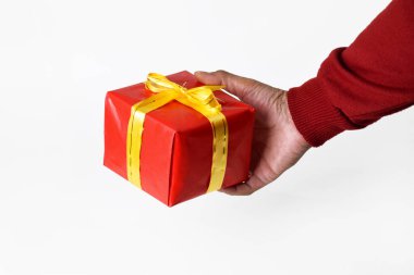 Kırmızı kazak giyen bir kişinin eli, beyaz arka planda sarı altın kurdeleli kırmızı bir hediye kutusu gösterir. Noel ve Yeni Yıl kutlamalarında