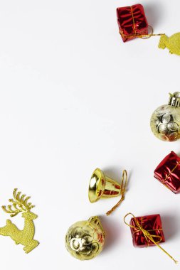 Altın toplar, kırmızı hediye kutuları ve sade beyaz bir yüzeye yerleştirilmiş altın bir zil de dahil olmak üzere bir Noel süslemeleri koleksiyonunun yakın çekimi..