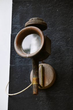 Eskimiş, paslı, yuvarlak cam mercekli metal bir duvar feneri, koyu taştan bir duvara monte edilmiş..