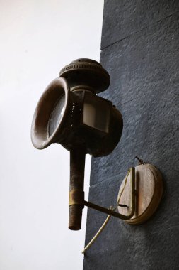 Eskimiş, paslı, yuvarlak cam mercekli metal bir duvar feneri, koyu taştan bir duvara monte edilmiş..