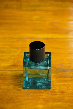 Pürüzsüz, açık kahverengi bir ahşap masaya yerleştirilmiş, mat siyah şapkalı, parlak bir deniz mavisi parfüm şişesinin detaylı bir yakın çekimi..