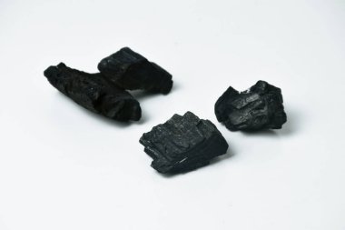 Yakıt olarak kullanılan, beyaz arka planda izole edilmiş, doğal ahşaptan yapılmış siyah kömür parçalarının yakın plan fotoğrafı..