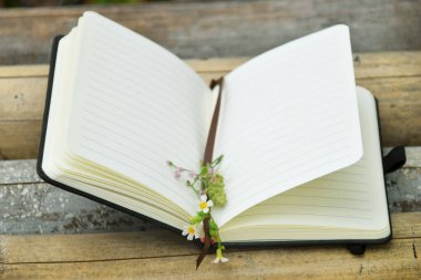 Bambu üzerine açık bir kitabın sayfaları arasındaki küçük sarı çiçeğin doğal bir arka planı var. Dünya Kitap Günü, doğa eğitimi ve açık hava okuma temaları için mükemmel..