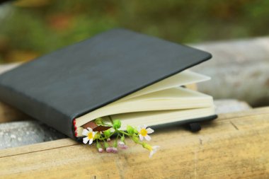 Bambuyla süslenmiş sarı çiçekli siyah bir defter, doğal bir arka plana ayarlanmış. Dünya Kitap Günü ve doğa temalı öğrenme için mükemmel..