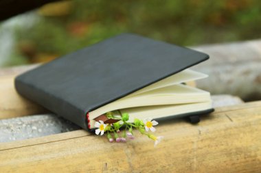 Bambuyla süslenmiş sarı çiçekli siyah bir defter, doğal bir arka plana ayarlanmış. Dünya Kitap Günü ve doğa temalı öğrenme için mükemmel..