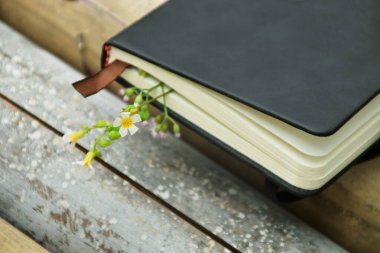 Bambuyla süslenmiş sarı çiçekli siyah bir defter, doğal bir arka plana ayarlanmış. Dünya Kitap Günü ve doğa temalı öğrenme için mükemmel..