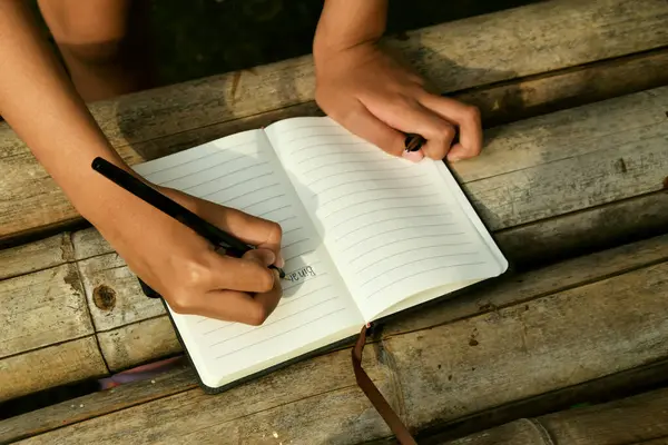 Bambu masasının üzerine doğal bir arka planı olan el yazısıyla yazılmış bir kitap. Doğa çalışmaları, geleneksel öğrenme ve Dünya Kitap Günü temaları için ideal.