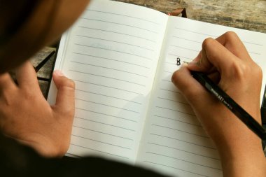 Bambu masa paspasına yerleştirilmiş açık bir kitaba yazı yazan bir kızın yakın çekimi. Öğrenim, eğitim, yaratıcılık, doğa ve Dünya Kitap Günü temaları için ideal