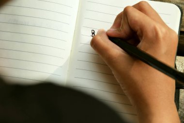 Bambu masa paspasına yerleştirilmiş açık bir kitaba yazı yazan bir kızın yakın çekimi. Öğrenim, eğitim, yaratıcılık, doğa ve Dünya Kitap Günü temaları için ideal.