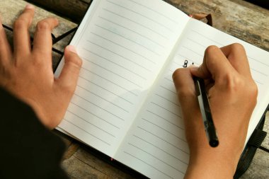 Bambu masasına yerleştirilmiş açık bir kitaba yazı yazan bir kızın üst görüntüsü. Doğa öğrenme, eğitim, yaratıcılık ve Dünya Kitap Günü temaları için mükemmel.