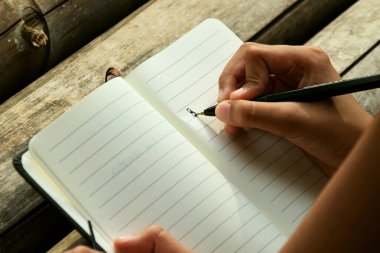 Bir çocuğun el yazısı, bambu masasının üzerine koyu, doğal bir arka plana yerleştirilmiş bir kitap. Doğa öğrenme, geleneksel eğitim ve Dünya Kitap Günü temaları için ideal.