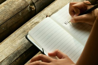 Bambu masasına yerleştirilmiş açık bir kitaba yazı yazan bir kızın üst görüntüsü. Doğa öğrenme, eğitim, yaratıcılık ve Dünya Kitap Günü temaları için mükemmel.