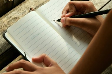 Bir çocuğun el yazısı, bambu masasının üzerine koyu, doğal bir arka plana yerleştirilmiş bir kitap. Doğa öğrenme, geleneksel eğitim ve Dünya Kitap Günü temaları için ideal.