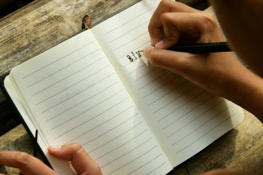 Bambu masasına yerleştirilmiş açık bir kitaba yazı yazan bir kızın üst görüntüsü. Doğa öğrenme, eğitim, yaratıcılık ve Dünya Kitap Günü temaları için mükemmel.