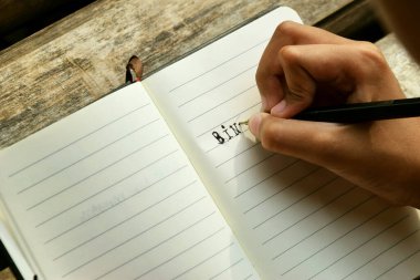 Bambu masa paspasına yerleştirilmiş açık bir kitaba yazı yazan bir kızın yakın çekimi. Öğrenim, eğitim, yaratıcılık, doğa ve Dünya Kitap Günü temaları için ideal