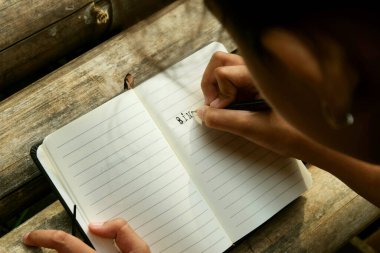 Bambu masa paspasına yerleştirilmiş açık bir kitaba yazı yazan bir kızın yakın çekimi. Öğrenim, eğitim, yaratıcılık, doğa ve Dünya Kitap Günü temaları için ideal