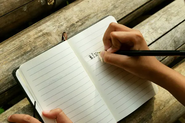 Bambu masa paspasına yerleştirilmiş açık bir kitaba yazı yazan bir kızın yakın çekimi. Öğrenim, eğitim, yaratıcılık, doğa ve Dünya Kitap Günü temaları için ideal