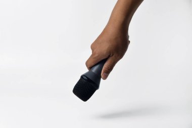 İzole edilmiş beyaz bir arkaplana karşı bir erkek elinin mikrofonu sıkıca tutuşu. Ses, şarkı söyleme, topluluk önünde konuşma, ifade özgürlüğü, direniş ve demokrasi kavramları için ideal.