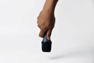 İzole edilmiş beyaz bir arkaplana karşı bir erkek elinin mikrofonu sıkıca tutuşu. Ses, şarkı söyleme, topluluk önünde konuşma, ifade özgürlüğü, direniş ve demokrasi kavramları için ideal.