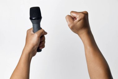 Bir kişi aşağıdan bir mikrofon tutar ve diğer el yukarı doğru sarılır ve beyaz izole bir arka plan oluşturur. Konuşma, şarkı söyleme, direniş ve demokrasinin sembolü.