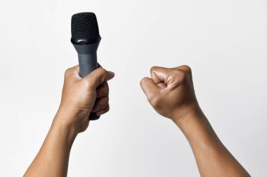 Bir kişi aşağıdan bir mikrofon tutar ve diğer el yukarı doğru sarılır ve beyaz izole bir arka plan oluşturur. Konuşma, şarkı söyleme, direniş ve demokrasinin sembolü.