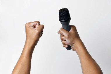 Bir kişi aşağıdan bir mikrofon tutar ve diğer el yukarı doğru sarılır ve beyaz izole bir arka plan oluşturur. Konuşma, şarkı söyleme, direniş ve demokrasinin sembolü.