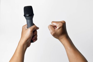 Bir kişi aşağıdan bir mikrofon tutar ve diğer el yukarı doğru sarılır ve beyaz izole bir arka plan oluşturur. Konuşma, şarkı söyleme, direniş ve demokrasinin sembolü.