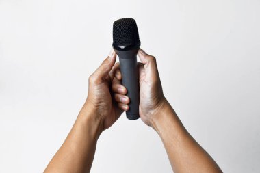 İzole edilmiş beyaz bir arka planda mikrofon tutan Asyalı bir adamın iki elinin yakın çekimi. Şarkı söylemenin, sesin, direnişin ve demokrasinin sembolü.