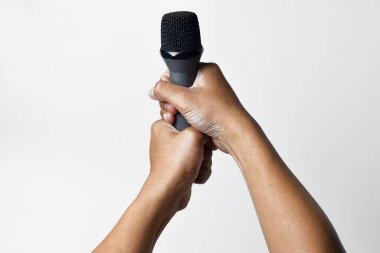 İzole edilmiş beyaz bir arka planda mikrofon tutan Asyalı bir adamın iki elinin yakın çekimi. Şarkı söylemenin, sesin, direnişin ve demokrasinin sembolü.