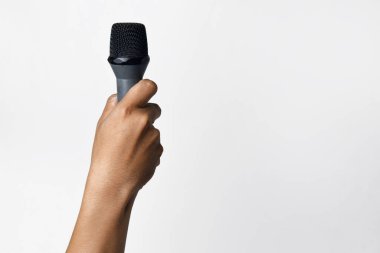 Asyalı bir adamın elinin beyaz izole edilmiş bir arka plana mikrofon tutarken yakın plan görüntüsü. Şarkı söyleme, konuşma özgürlüğü, ifade özgürlüğü, direniş ve demokrasi kavramı.
