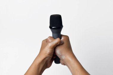 İzole edilmiş beyaz bir arka planda mikrofon tutan Asyalı bir adamın iki elinin yakın çekimi. Şarkı söylemenin, sesin, direnişin ve demokrasinin sembolü.