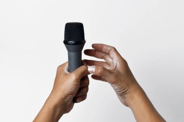 İzole edilmiş beyaz bir arka planda mikrofon tutan Asyalı bir adamın iki elinin yakın çekimi. Şarkı söylemenin, sesin, direnişin ve demokrasinin sembolü.