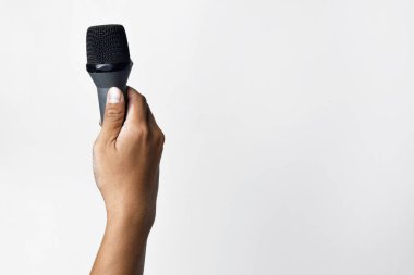 Asyalı bir adamın elinin beyaz izole edilmiş bir arka plana mikrofon tutarken yakın plan görüntüsü. Şarkı söyleme, konuşma özgürlüğü, ifade özgürlüğü, direniş ve demokrasi kavramı.