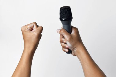 Bir kişi aşağıdan bir mikrofon tutar ve diğer el yukarı doğru sarılır ve beyaz izole bir arka plan oluşturur. Konuşma, şarkı söyleme, direniş ve demokrasinin sembolü.