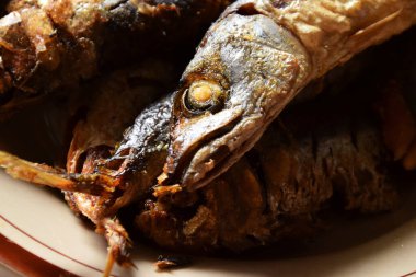 Birkaç geleneksel Endonezya kızarmış balığının balık kafaları izole edilmiş krema arkaplanlı bir tabakta servis ediliyor..