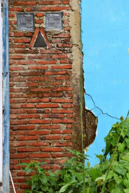 Yanında açık mavi duvarlar olan tuğla bir duvar evin arkasında açıkça görülüyor..