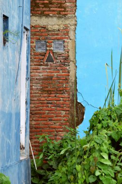 Yanında açık mavi duvarlar olan tuğla bir duvar evin arkasında açıkça görülüyor..