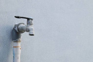 Kırılgan ve kirlenmeye başlayan bir musluk ve beyaz bir duvar arkaplanı.