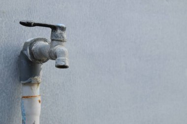 Kırılgan ve kirlenmeye başlayan bir musluk ve beyaz bir duvar arkaplanı.