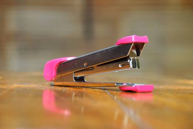 Kapat. Zımba kağıdını zımbalamak için kullanılan pembe zımba arka planda bambu perdesi olan ahşap bir masada oturur..