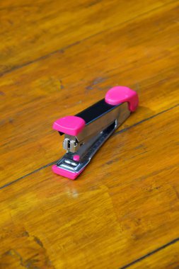 Kağıtları zımbalamak için kullanılan pembe zımba ahşap bir masaya oturur..