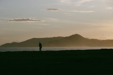 Kumsalda sırt çantalı bir adamın silueti.
