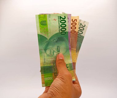 Kediri, Endonezya - 1 Ekim 2023: 20.000, 10000, 5000 ve 2000 rupilik banknotlar beyaz arka planda izole edilmiş erkek eli