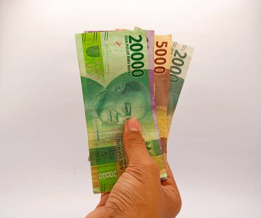 Kediri, Endonezya - 25 Ekim 2023: erkek eli 20.000, 10000, 5000 ve 2000 rupiah banknotları beyaz arka planda izole edilmiş.