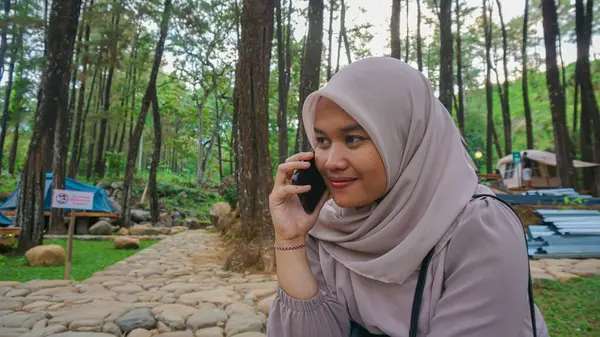 Parkta otururken telefonla konuşan neşeli genç bir kadının portresi.