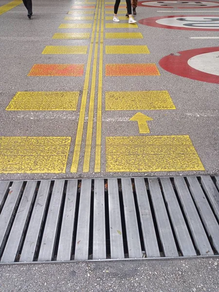 Pedestrian crossing lines, channel grids and speed limit sign. A few people crossing across.