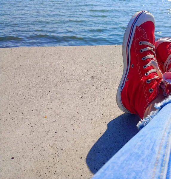 Rode Sneakers Jeans Het Meisje Zit Tegenover Zee Kopieerruimte — Stockfoto